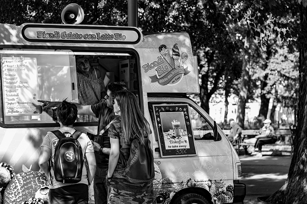 black and white photo of a gelato food truck in a park with customers discussing the menu