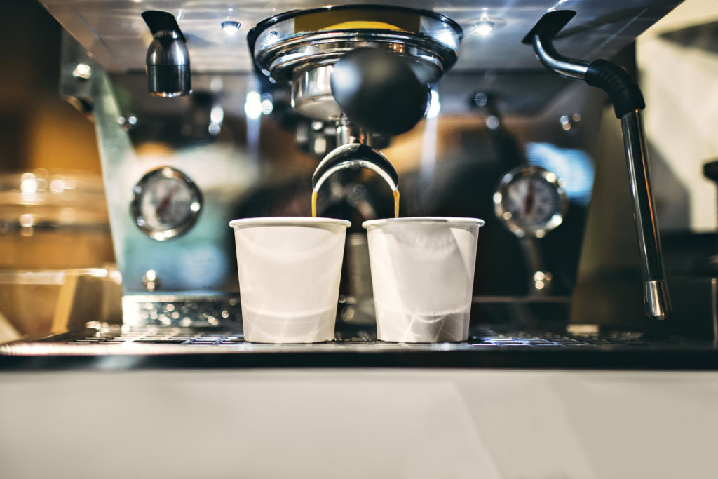 photo of a small espresso machine brewing espresso coffee into two small white cups in a coffee shop