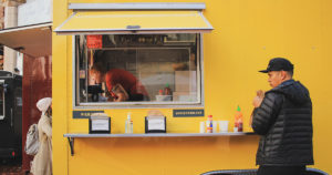 patrons getting food from a yellow food trailer